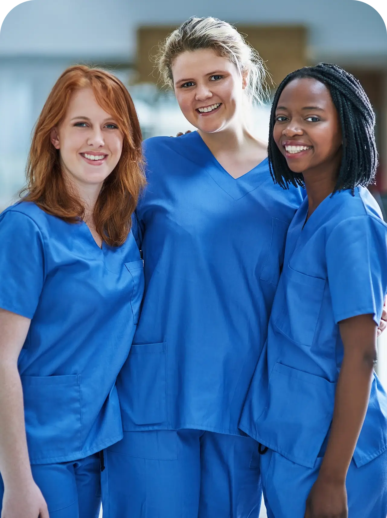 Three nurses smiling in blue uniforms.